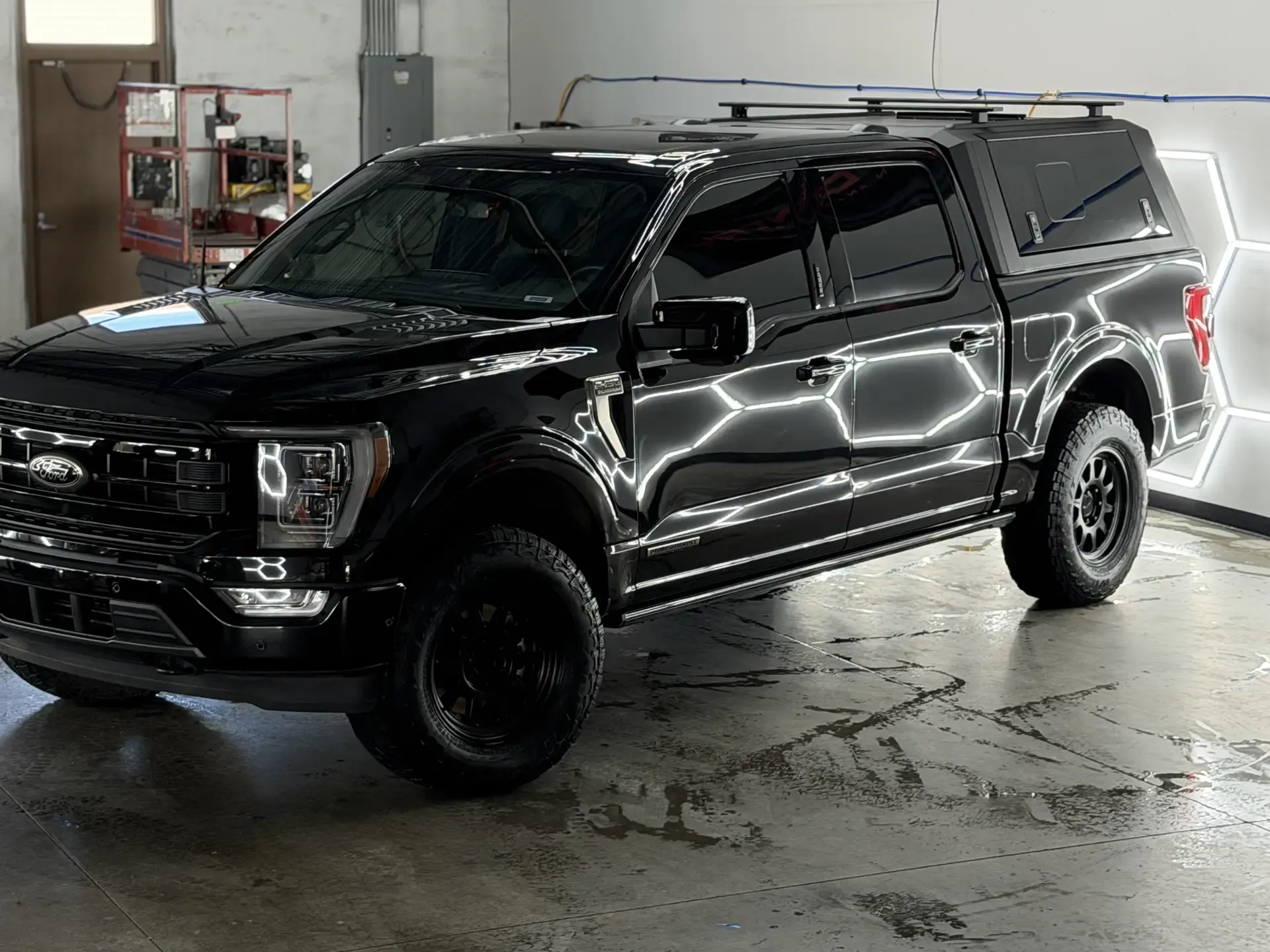A black Ford F-150 Platinum with a color-matched cap and roof rack under the studio's hexagon lights
