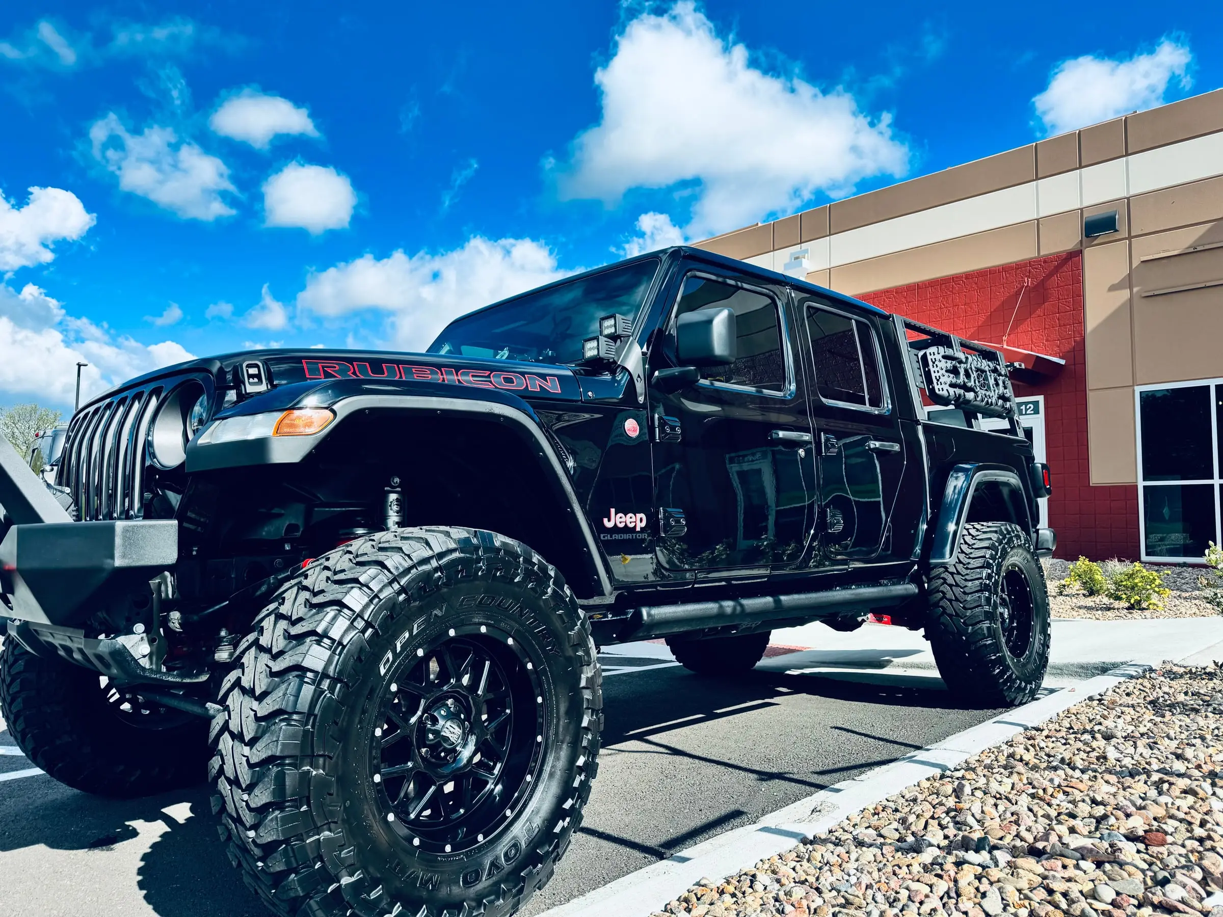 A black Jeep Wrangler Rubicon on off-road tires parked outside the Ride N' Shine storefront after a detail