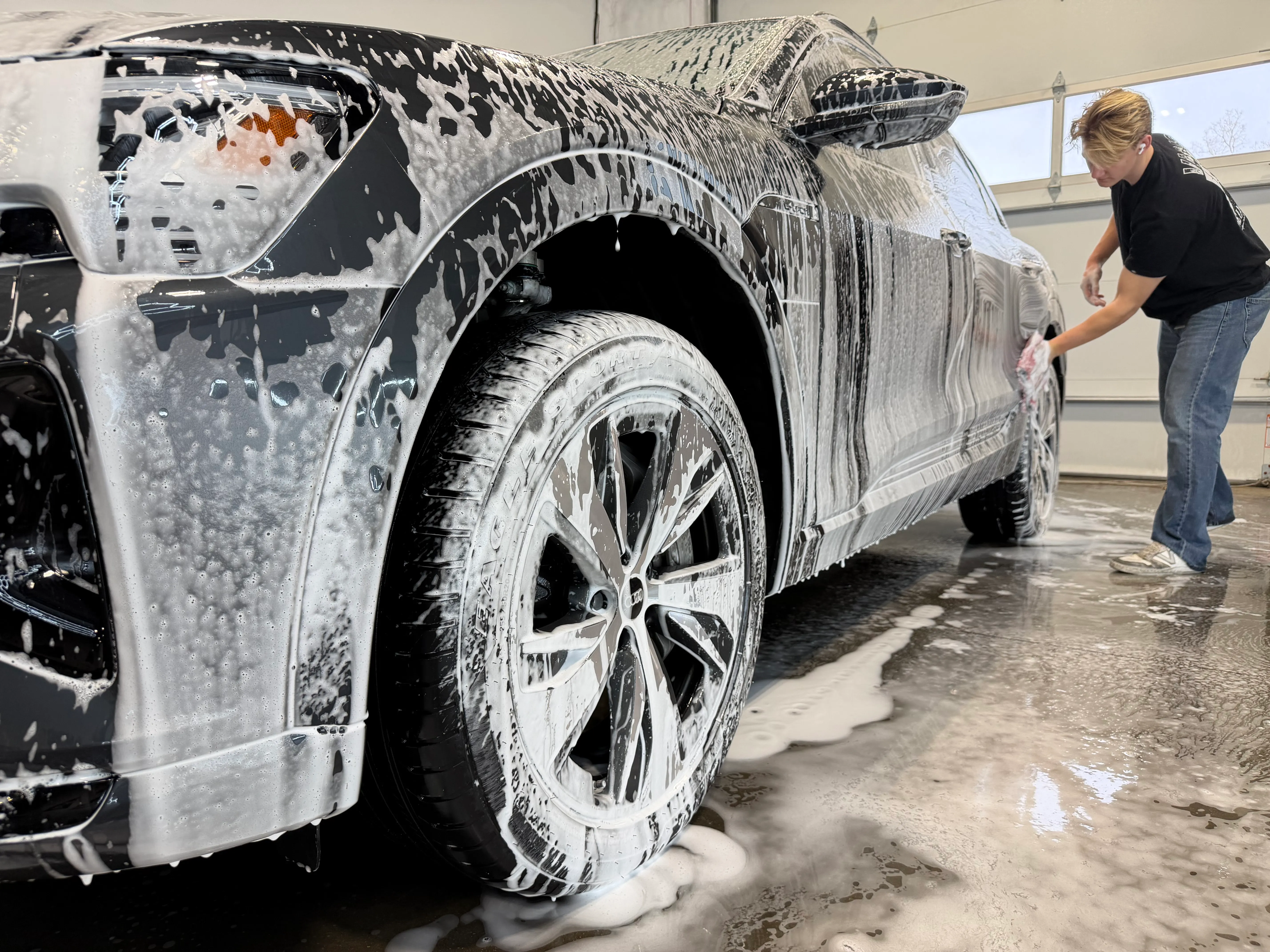 A technician washing a foam-covered Audi SUV in the wash bay