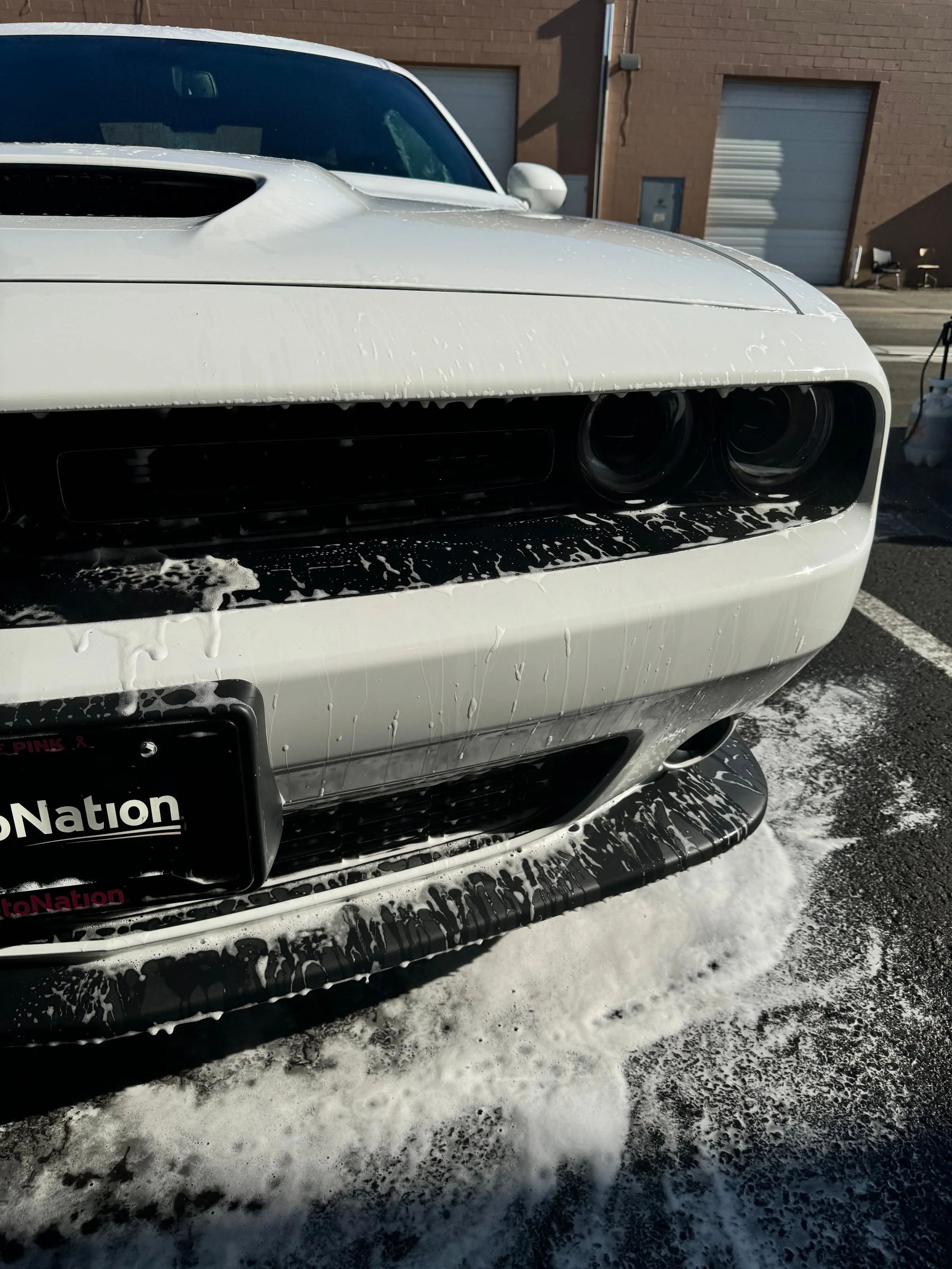 The front end of a white Dodge Challenger running with suds outside the shop