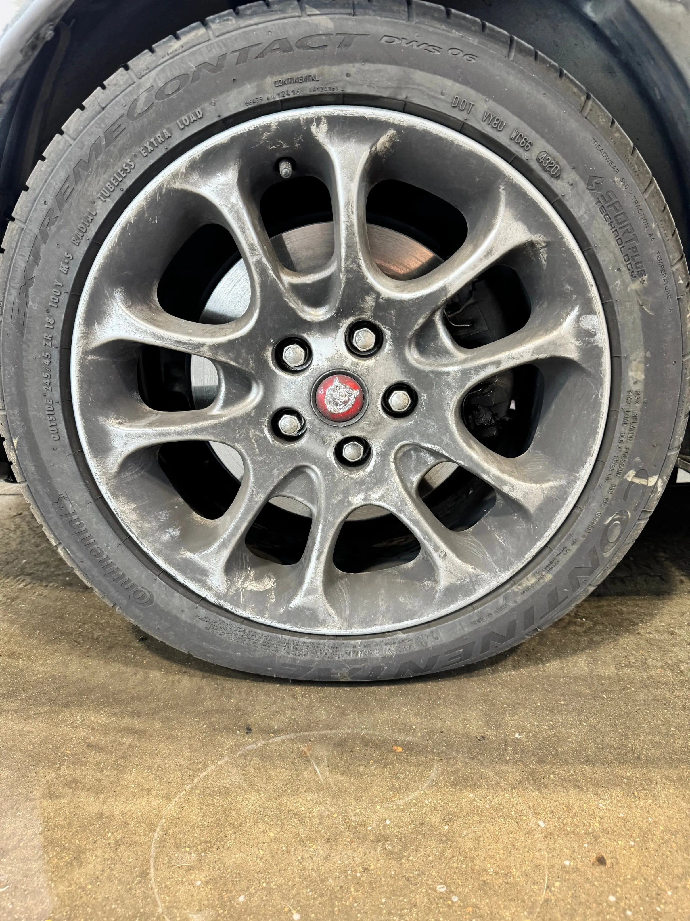 A silver alloy wheel dulled by brake dust, its red centre cap barely legible