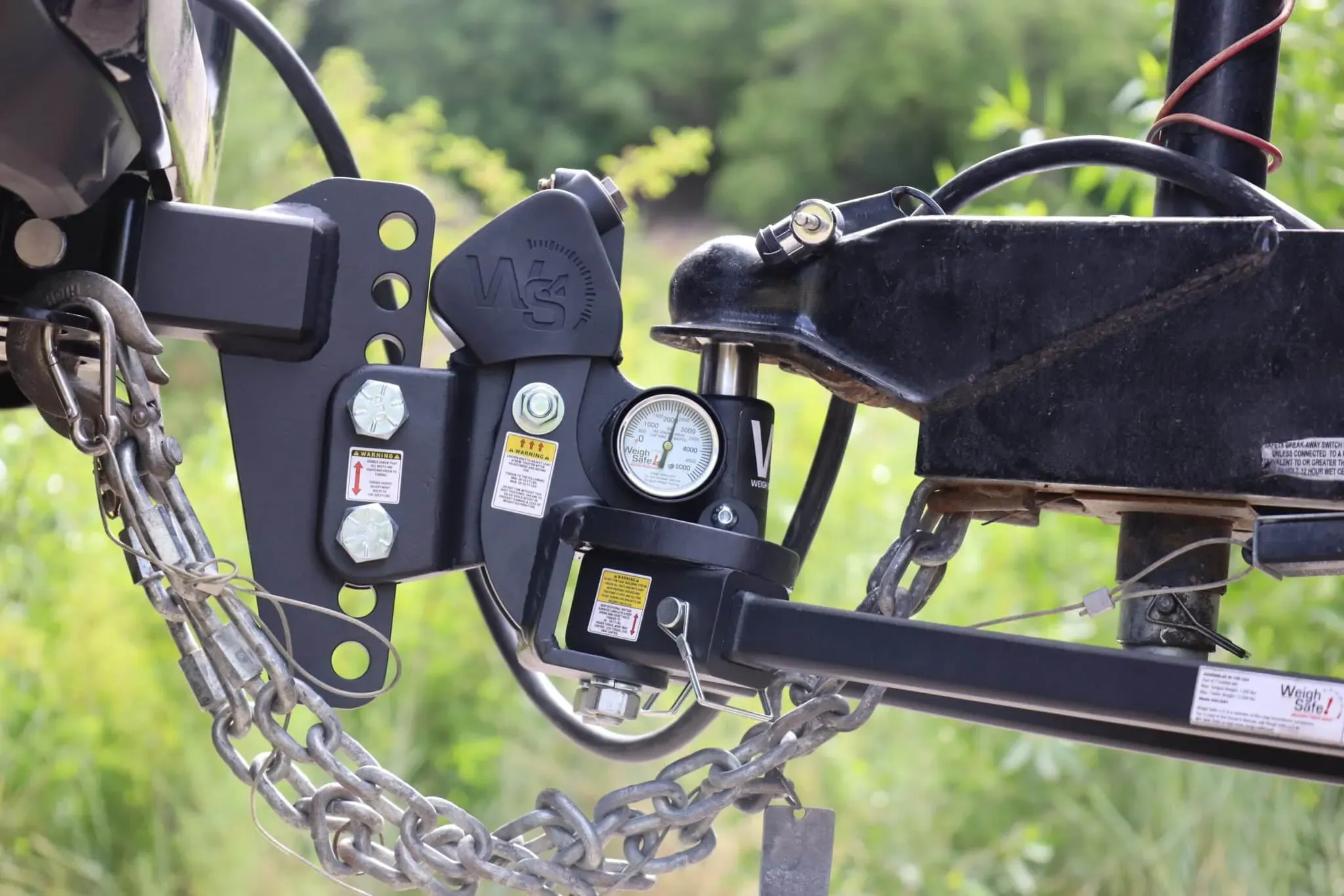 A coupler latched over the ball of an adjustable hitch, with safety chains crossed underneath, the breakaway cable run to the receiver, and the pin and clip in place
