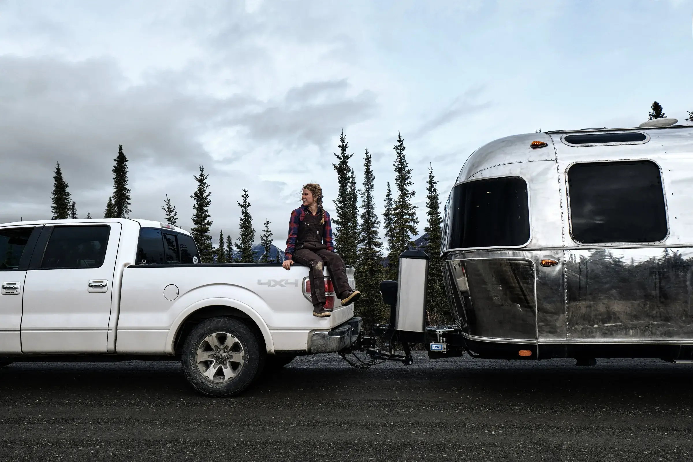 A white Ford F-150 hitched to an Airstream travel trailer on a gravel pullout, the trailer sitting level behind the truck