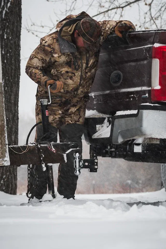 A person in winter gear working the tongue jack of a trailer hitched to a Ford Super Duty during snowfall