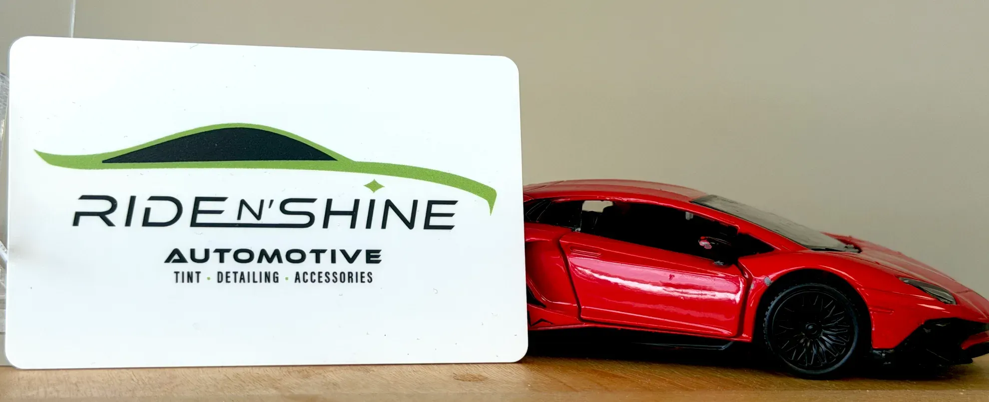 A Ride N' Shine Automotive gift card propped beside a red model car on a wooden shelf