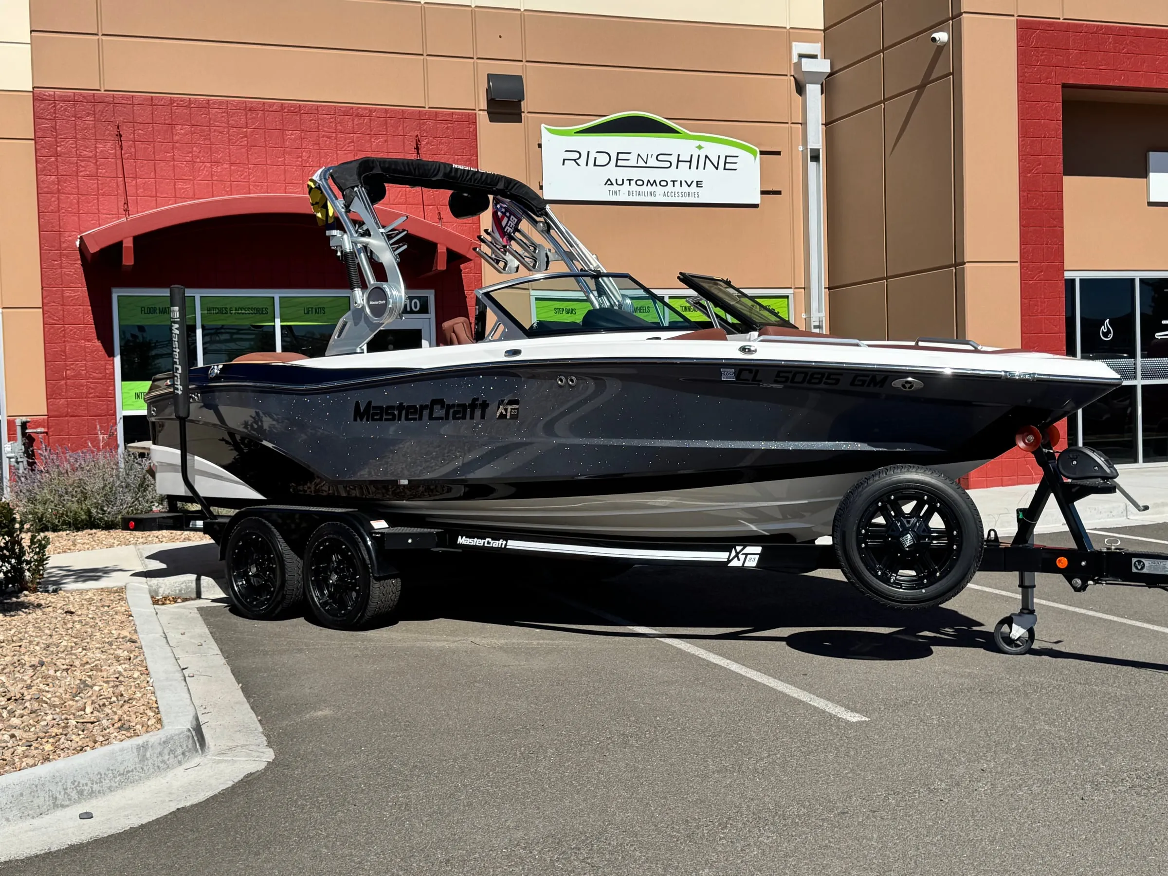 A black MasterCraft XT23 on its trailer outside the Ride N' Shine storefront, its metalflake hull polished to a gloss