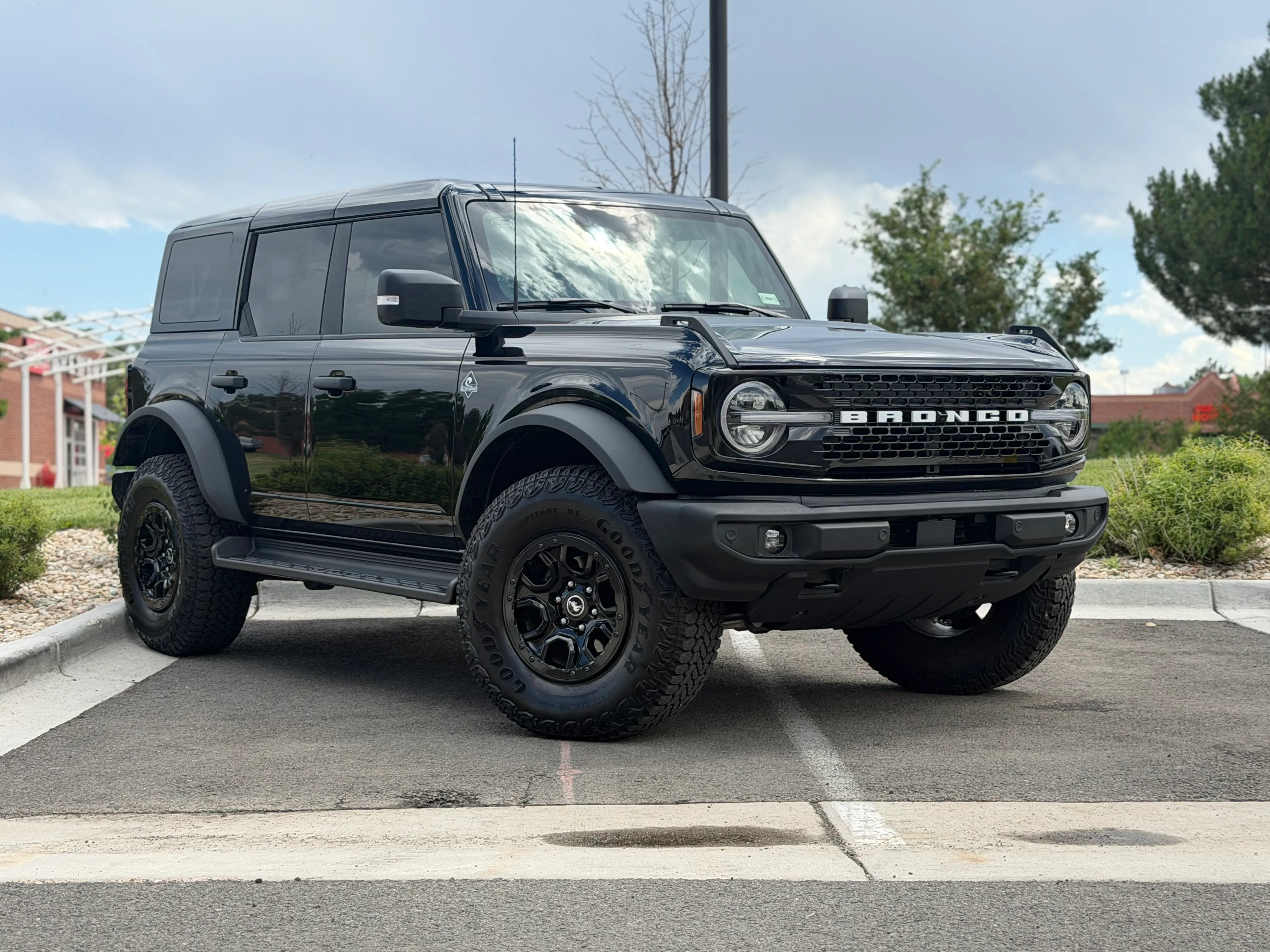 A black four-door Ford Bronco parked outside the shop on a cloudy day, seen from the front three-quarter angle