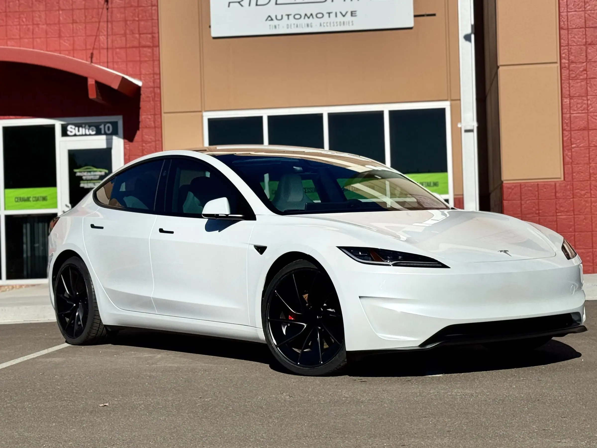 A white Tesla Model 3 Performance on black wheels parked in front of the Ride N' Shine storefront in Arvada