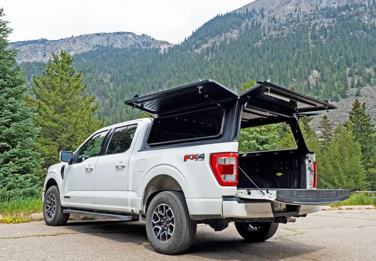 A white Ford F-150 with a WanderFox Super Den aluminum topper, its gullwing side door open, in the mountains (WanderFox photo)