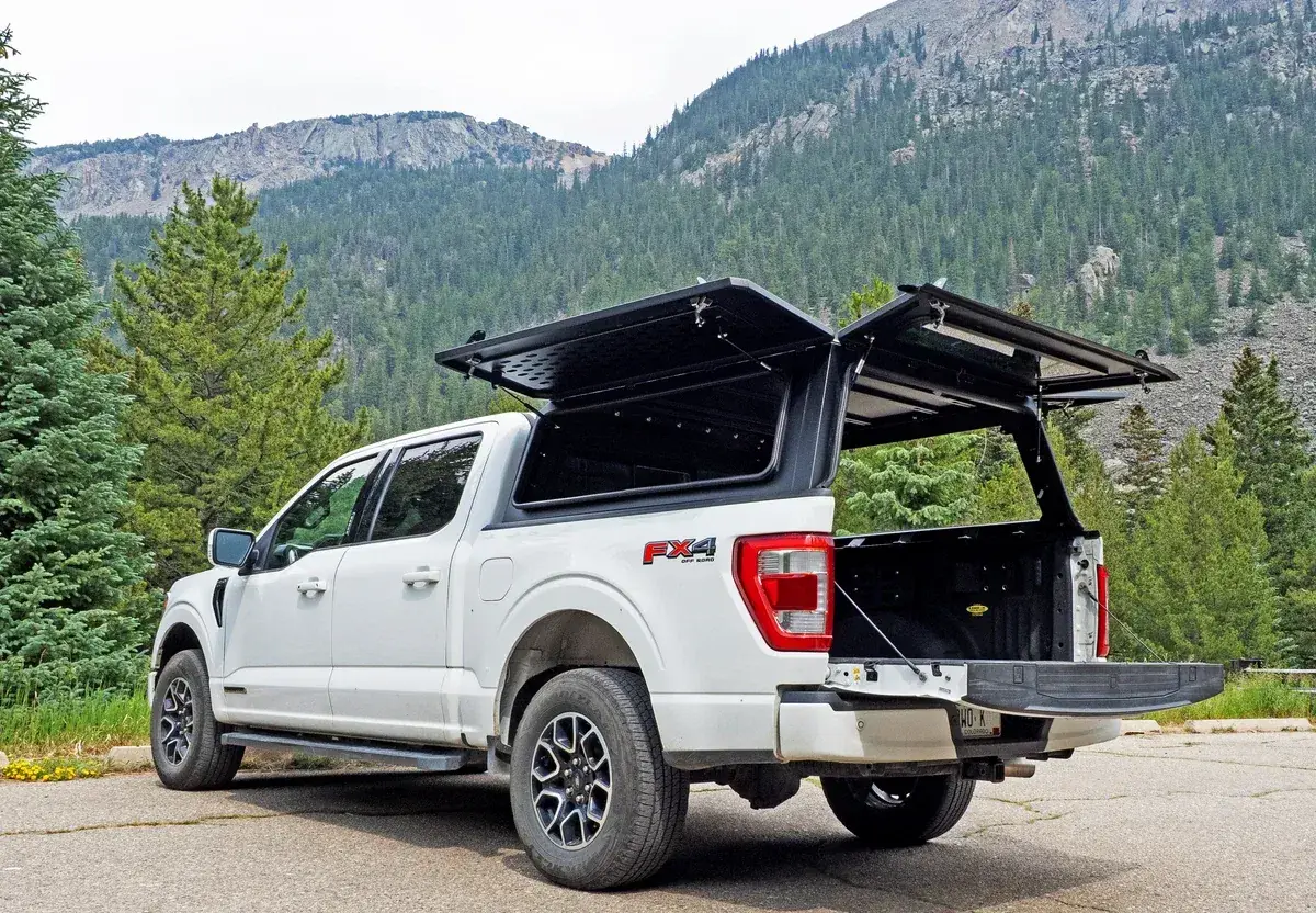 A white Ford F-150 with a WanderFox Super Den aluminum topper, its gullwing side door open, in the mountains (WanderFox photo)