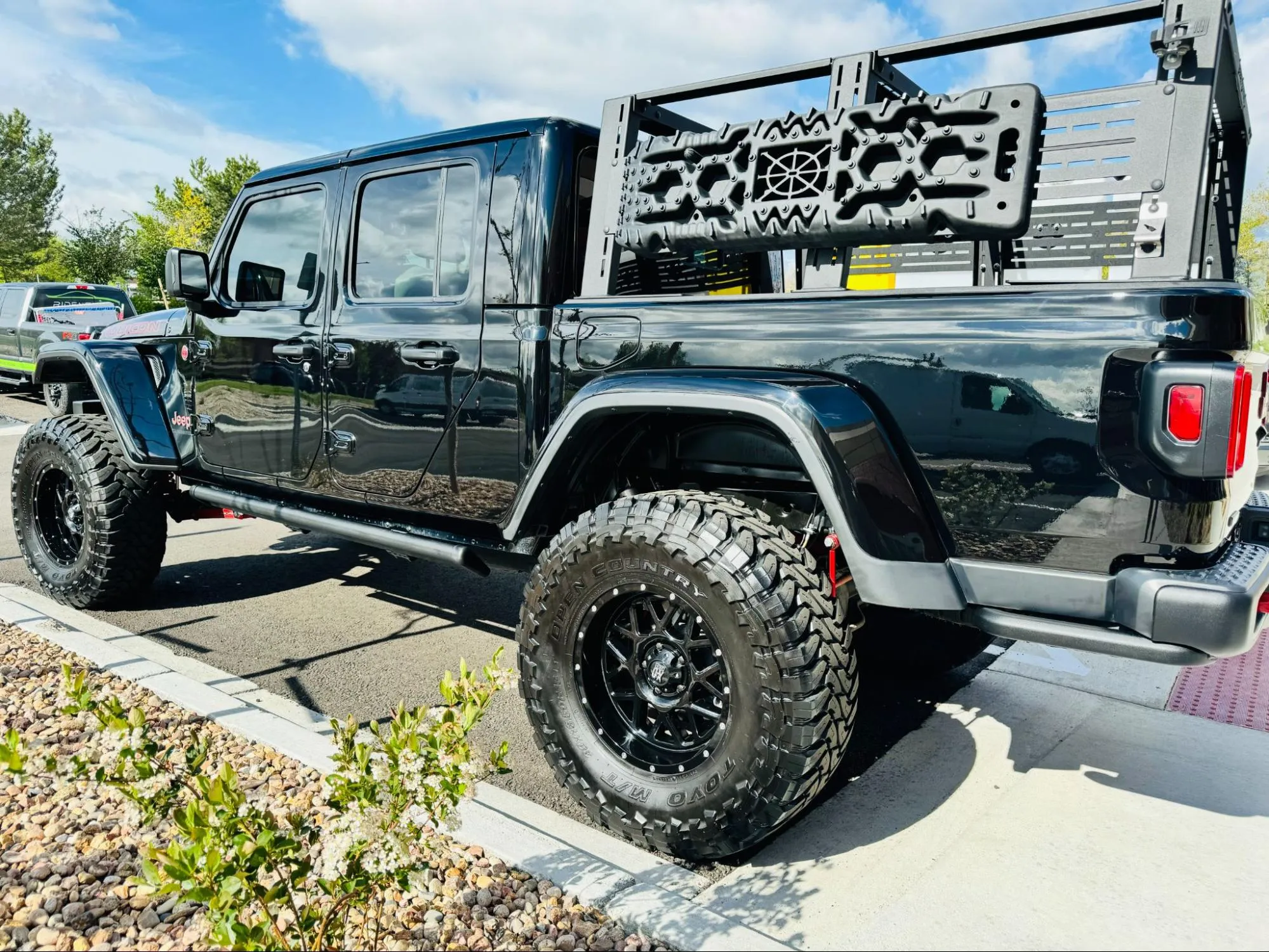 A black Jeep Gladiator with a bed rack, fender flares, and Toyo M/T tires parked outside Ride N' Shine