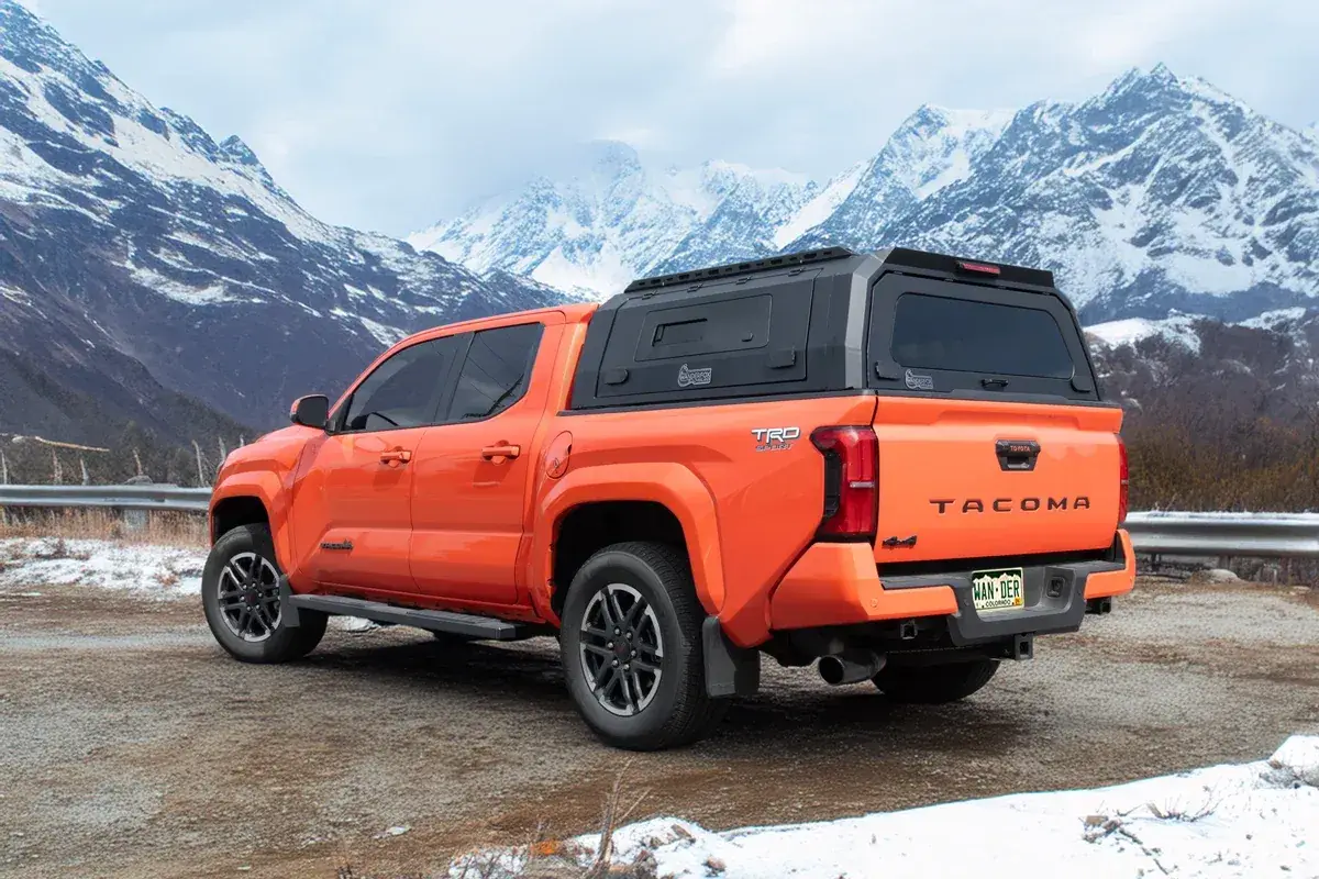 An orange Toyota Tacoma with a WanderFox Den topper parked below snowy peaks (WanderFox photo)