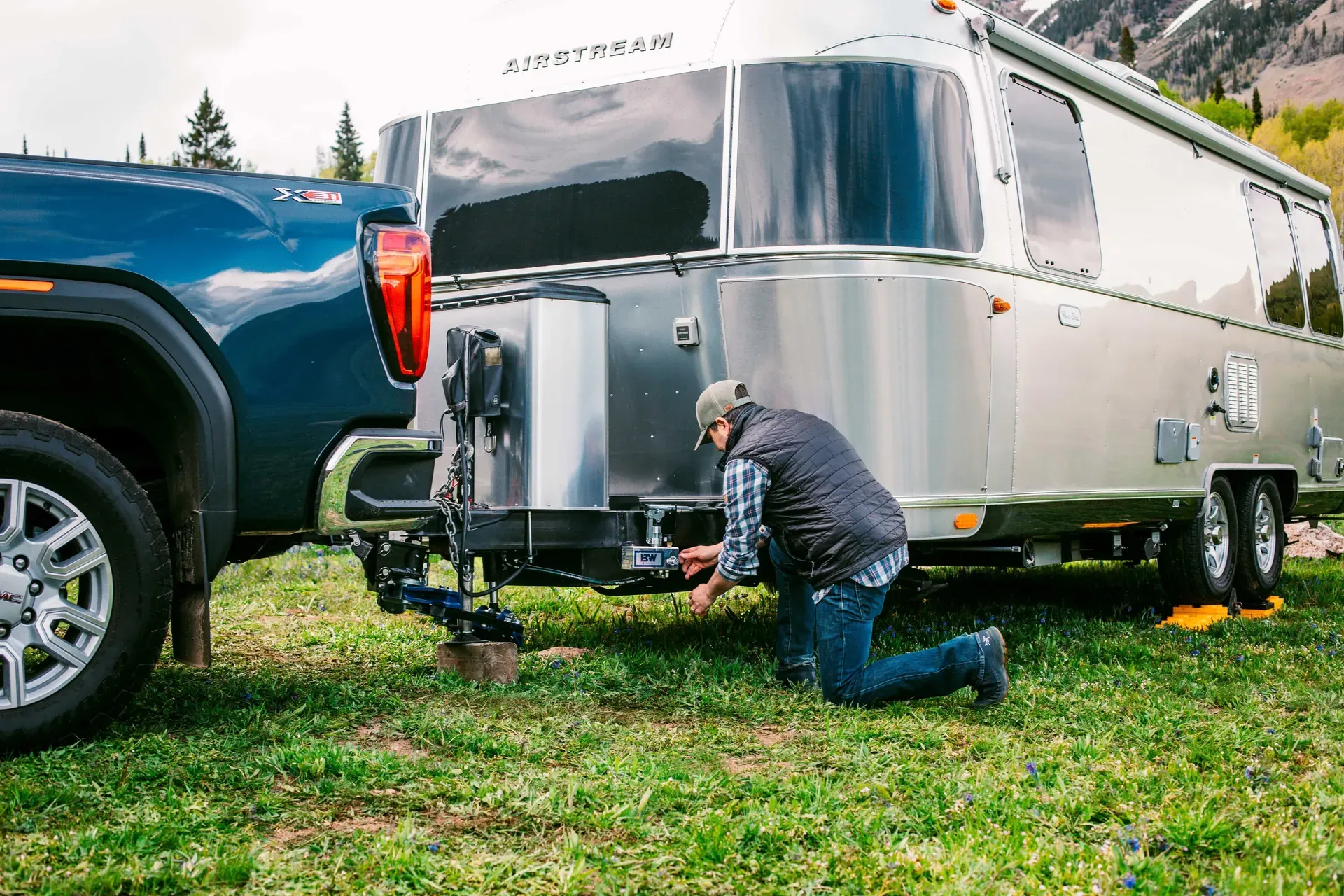 A man setting up a weight distribution hitch between a pickup and an Airstream trailer (B&W photo)