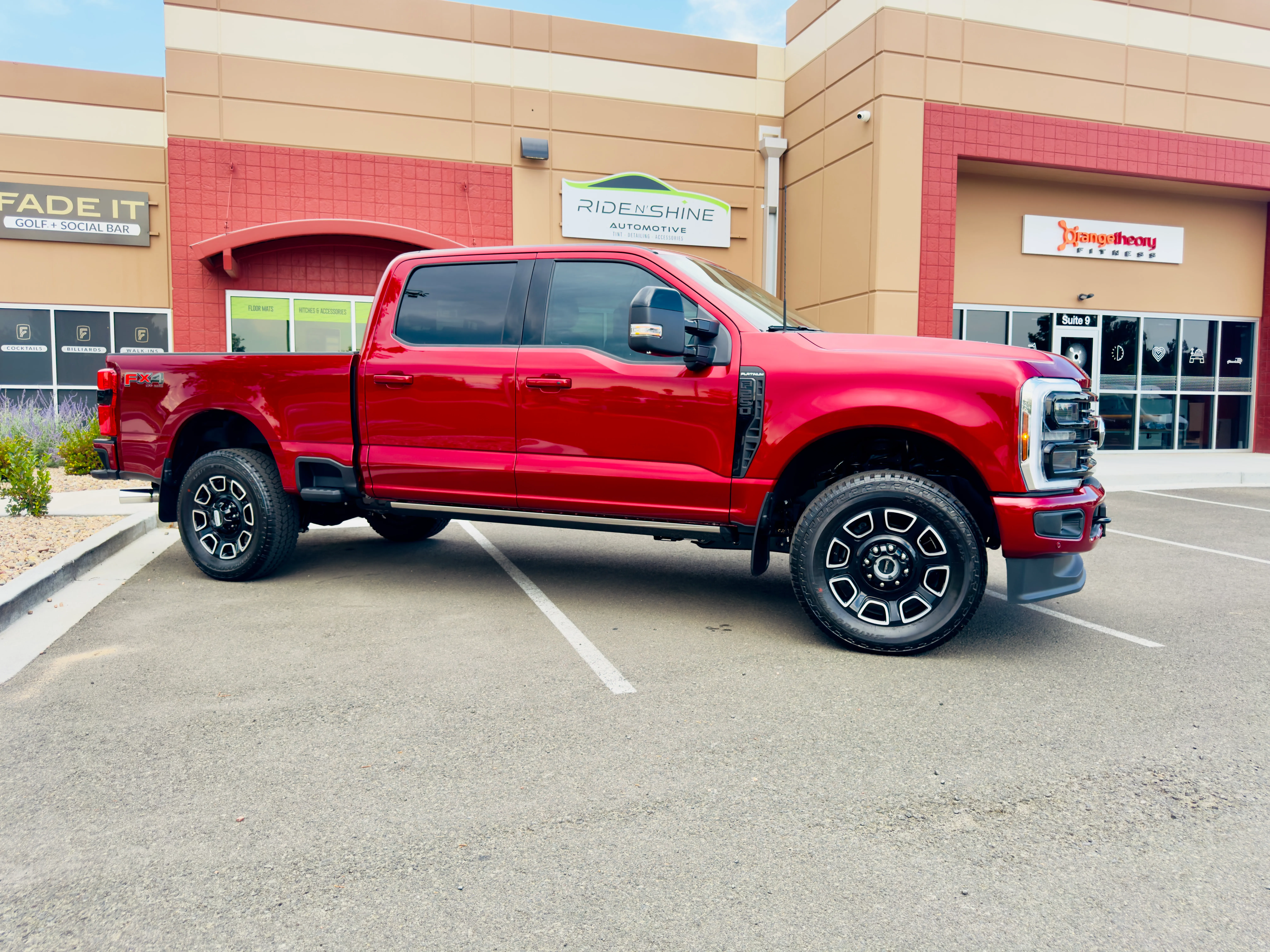 A red Ford F-250 Super Duty crew cab parked outside the Ride N' Shine storefront in Arvada