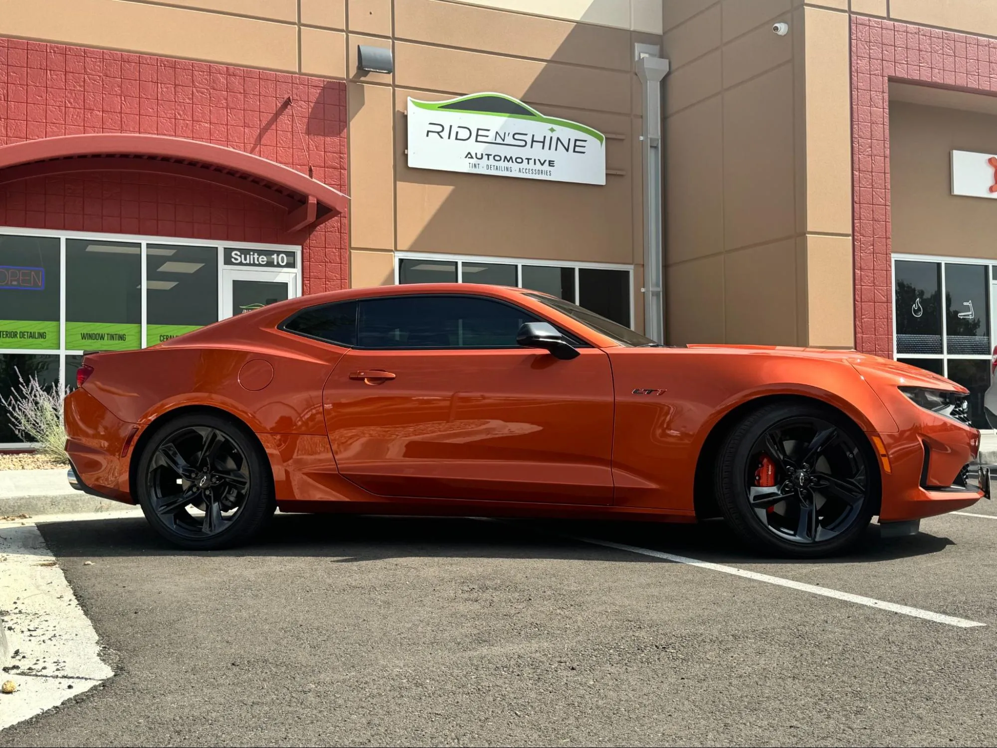 An orange Chevrolet Camaro LT1 with tinted windows parked outside the Ride N' Shine storefront