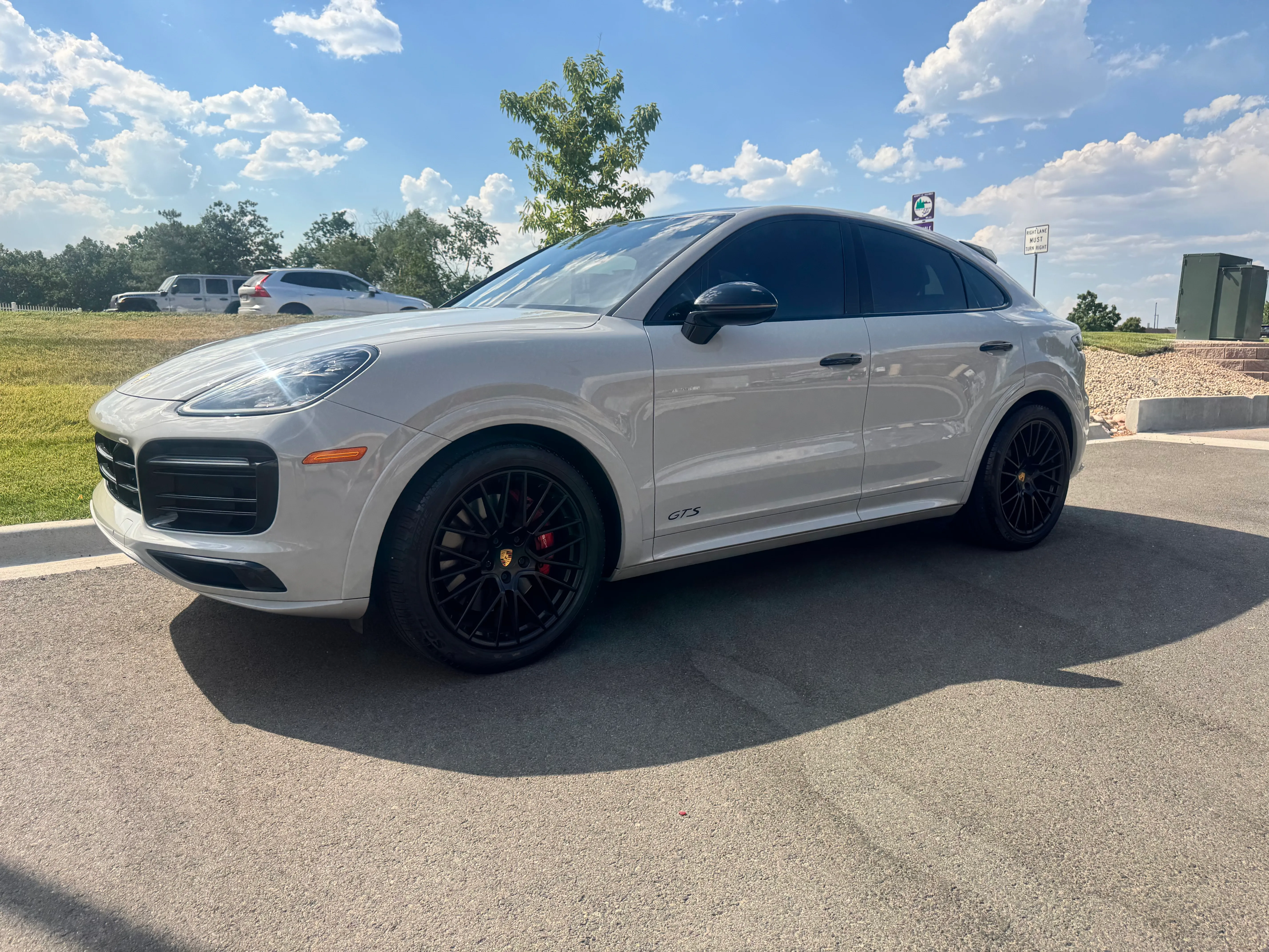 A chalk grey Porsche Cayenne Coupe GTS with tinted windows parked in a lot under a blue sky