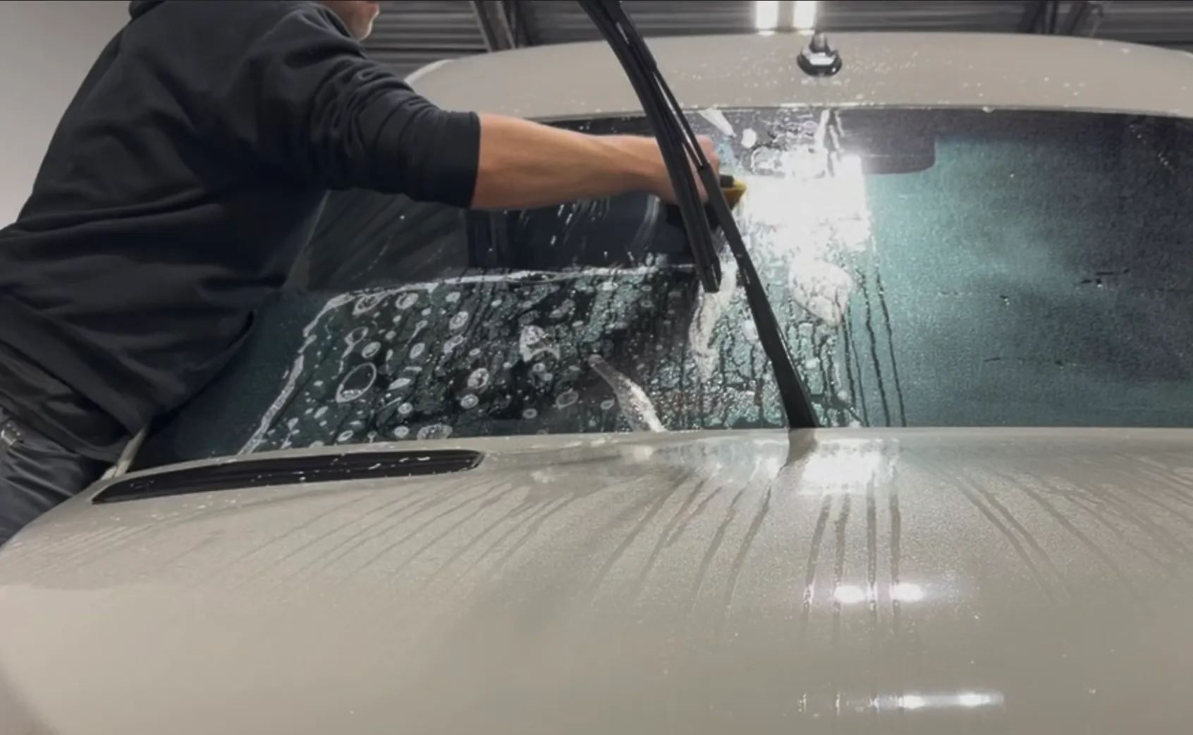 A technician applies protective film to a car's windshield with a soapy solution
